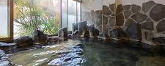 石を組んだ湯船。大きな窓の外に木々の緑。